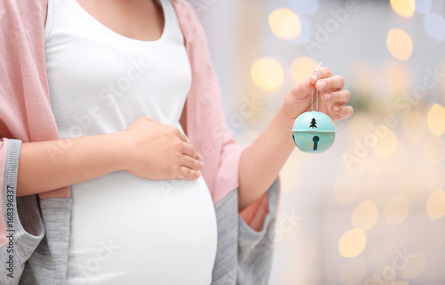 Young pregnant woman with Christmas jingle bell at home