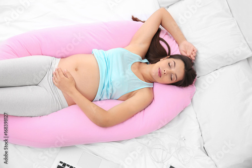 Young pregnant woman sleeping on maternity pillow in bed