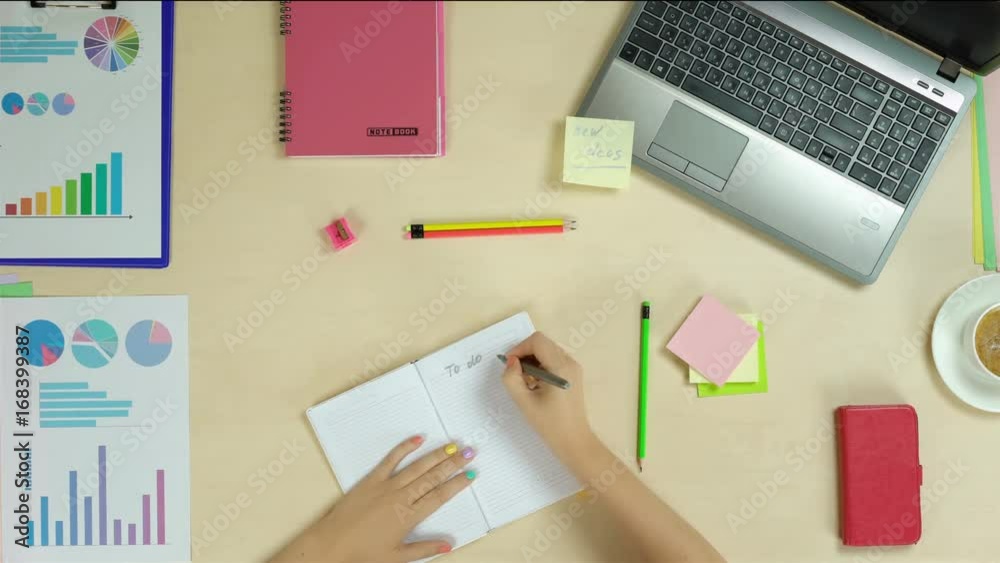 Person writing to do list at work, self employed woman planning a day, startup. Top view of female hands working, writing down in notebook