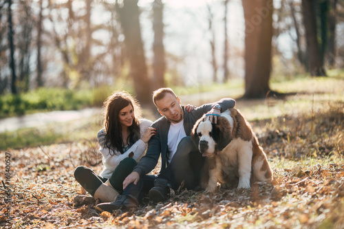 Young couple enjoying nature outdoors together with their adorable Saint Bernard puppy. People and dogs theme.