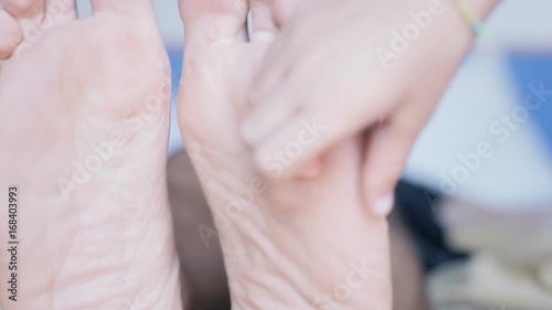 The hand of a child tickling the feet of a man resting on the bed. Close-up detail front shot.
