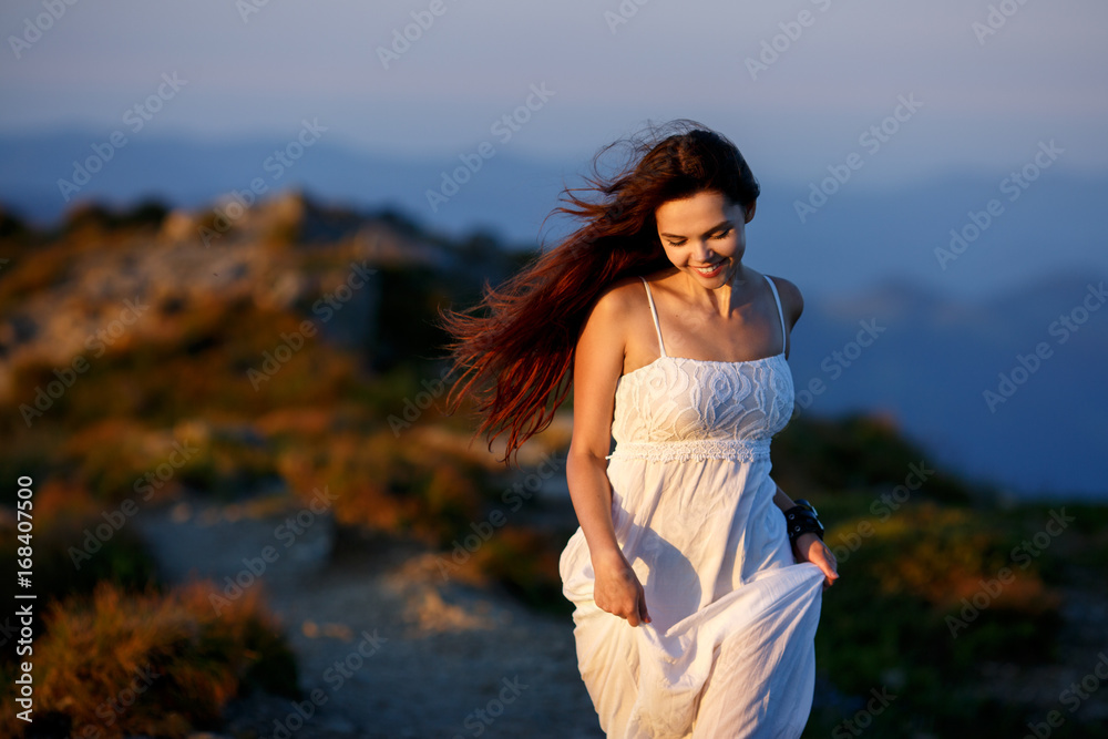 Beautiful woman in white dress running in the mountains. Jumping on mountain peak rock. Beautiful girl looking happy and smiling. Relaxing, feeling alive, breathing fresh air, got freedom from work Beautiful woman in white dress running in the mountains. Jumping on mountain peak rock. Beautiful girl looking happy and smiling. Relaxing, feeling alive, breathing fresh air, got freedom from work