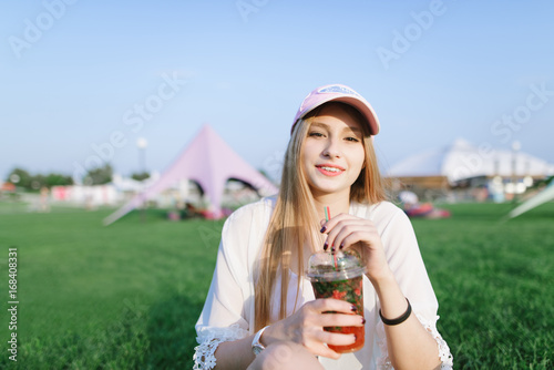 Portrait of a beautiful smiling girl with a refreshing drink in her arms resting in the park. Summer concept.