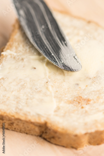 Closeup macro bread coated with butter on the wooden board with knife
