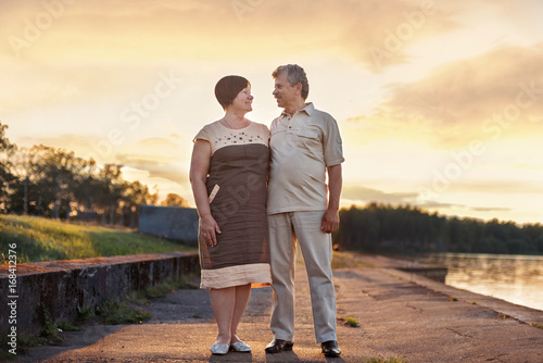 Elderly couple walking talking laughing at the sunset near the lake river
