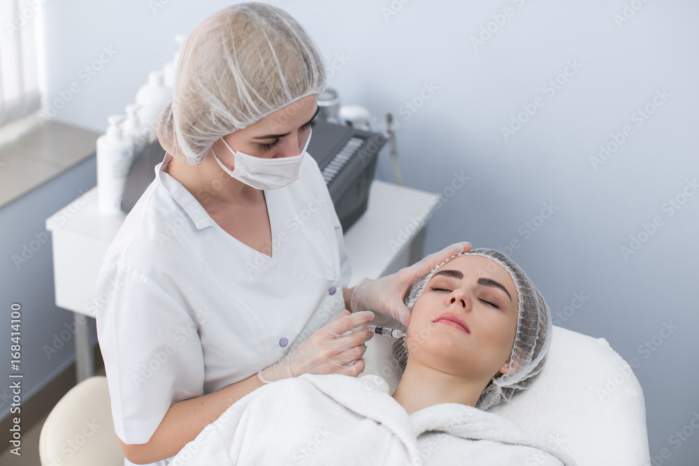 Woman gets injection in her face. Beauty woman giving botox injections. Young woman gets beauty facial injections in the cosmetology salon. Face aging injection. Aesthetic Medicine, Cosmetology Woman gets injection in her face. Beauty woman giving botox injections. Young woman gets beauty facial injections in the cosmetology salon. Face aging injection. Aesthetic Medicine, Cosmetology