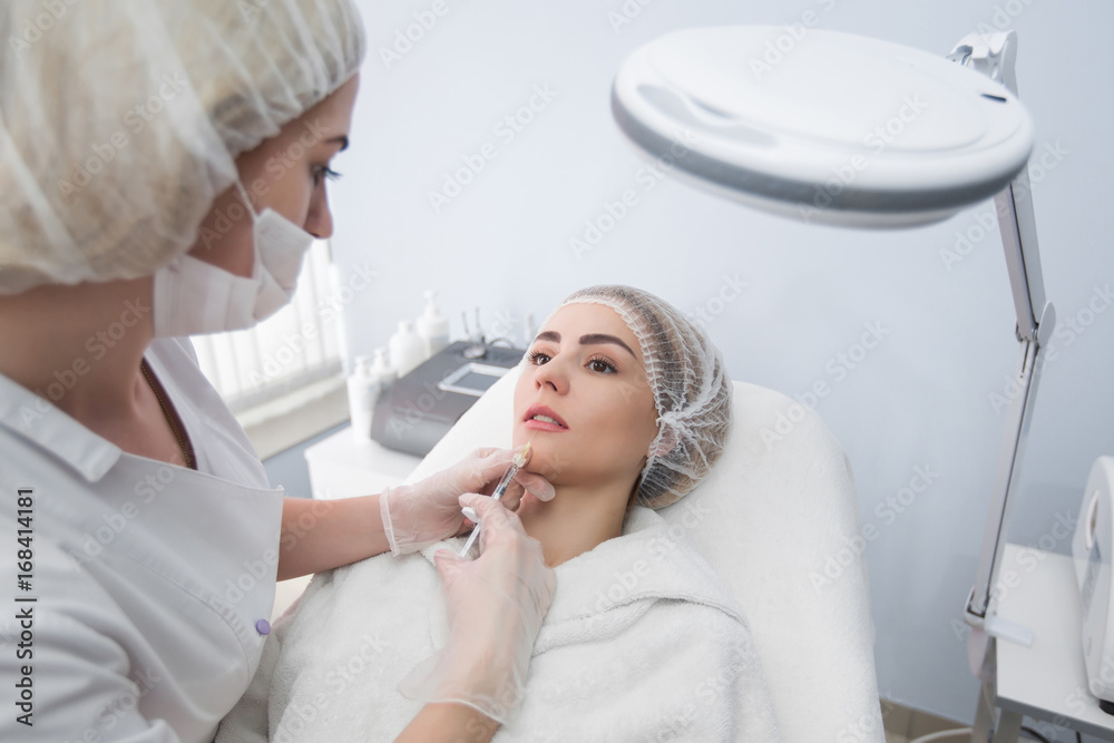 Hands of cosmetologist making injection in face, lips. Young woman gets beauty facial injections in salon. Face aging, rejuvenation and hydration procedures. Aesthetic cosmetology. Hands of cosmetologist making injection in face, lips. Young woman gets beauty facial injections in salon. Face aging, rejuvenation and hydration procedures. Aesthetic cosmetology.