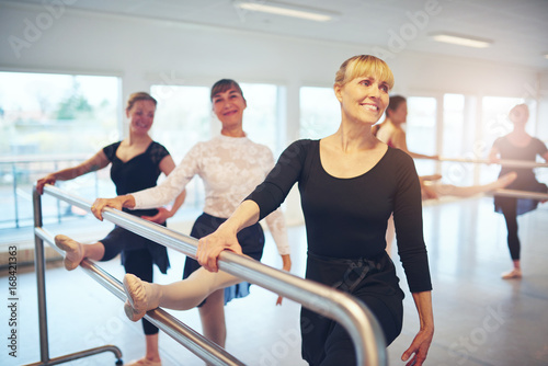 Smiling adult women standing at handrail and stretching in class