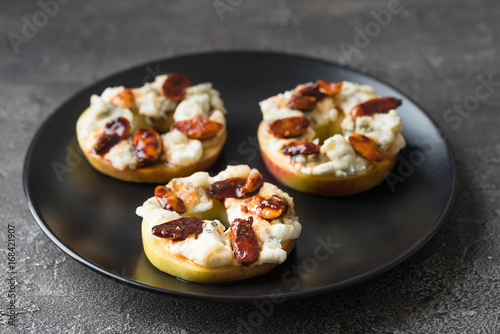 Apple circles with cream cheese, gorgonzola and spicy almond nuts with honey. Dark background