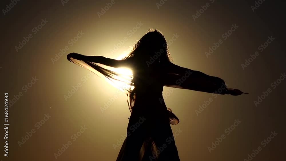 Girl with a veil in her hands dancing belly dance on the beach. Silhouette. Slow motion
