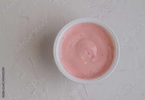 Healthy strawberry fruit flavored yogurt with natural coloring in plastic cup isolated on white rustic background - top view shot in studio
