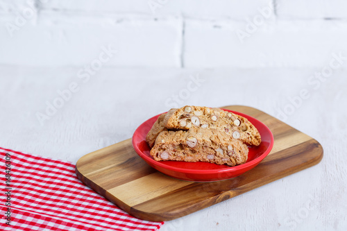 Cantucci. Typical Italian cookies on a saucer of red color and on a white wooden background