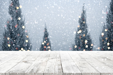 Christmas and New year background with wooden deck table over christmas tree, snow and blurred light bokeh. Empty display for product montage. Rustic vintage Xmas background.