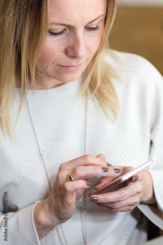 Young blond hair business woman writing a text message using messenger on smart phone photo