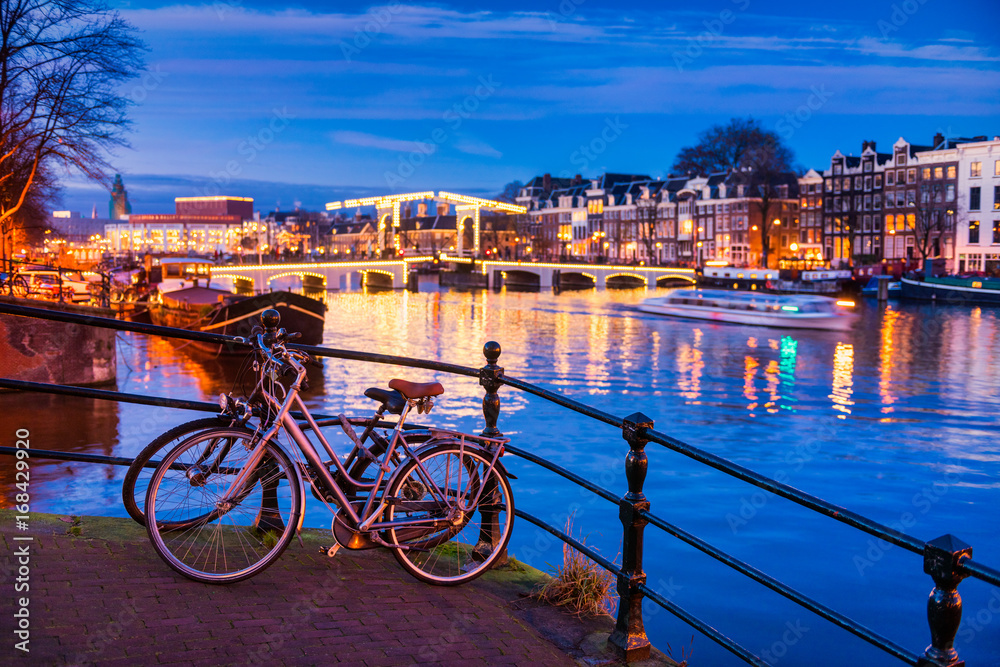 Skinny bridge and Amstel river in Amsterdam Netherlands at Dusk, selective foreground focus on bicycles