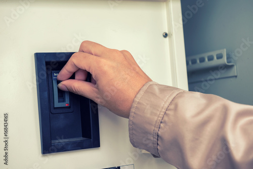 Man's hand with finger on light switch, about to turn off the lights. Closeup of hand and switch only. Horizontal format.