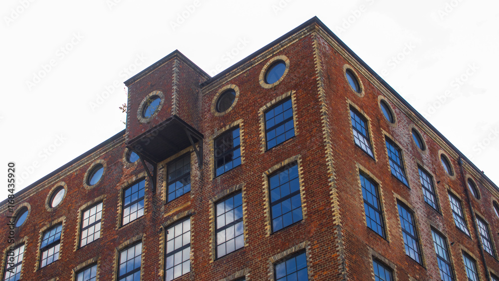 Brown brick building with old style windows reflecting blue sky and white clouds