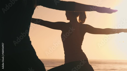 Group of 3 women practicing yoga on the beach against the sunset. Three black silhouettes of their bodies making yoga postures. Sun and the ocean creates ethereal & pure scene