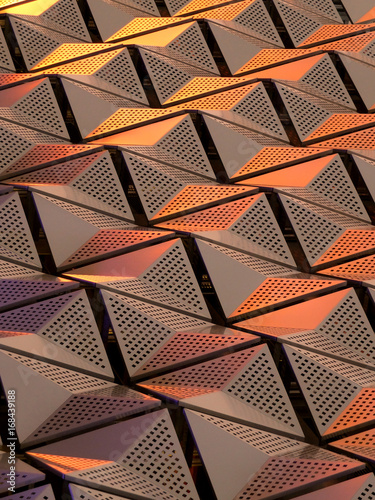 metallic geometric cladding or panels in copper and gold colours with repeating angular pattern