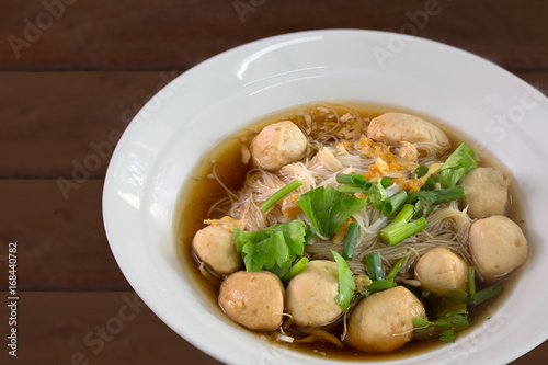 White noodle with pork ball with herb Chinese soup in white bowl on brown wooden background thai food