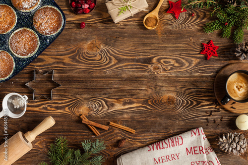 Christmas cookies with fir-tree branch on old wooden background. Cookies, black cup, candle, cupcakes, cone, cinnamon, wooden spoon, gift, branches of fir-tree. Copy space. Top view
