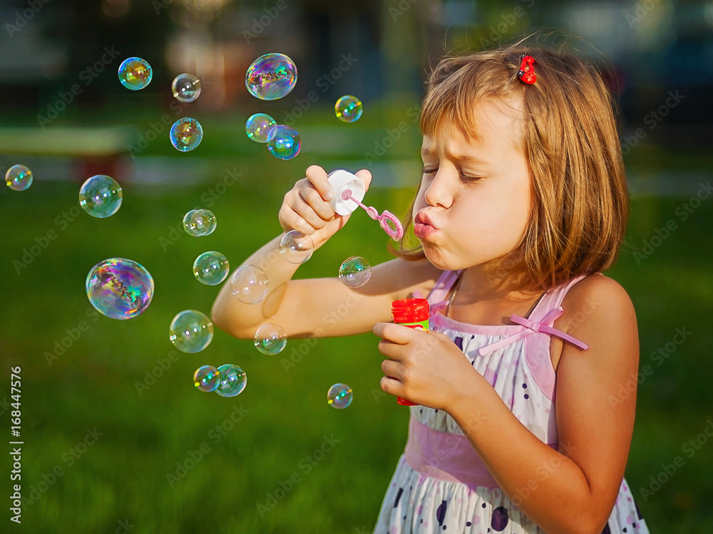 Cute little girl biowing soap bubbles.