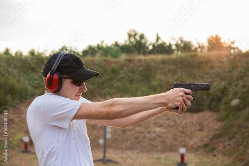 Young blond handsome secret service agent soldier training military camp firing gun desert eagle pistol at the target in the distance and kill full body equipment professional assassin in nature