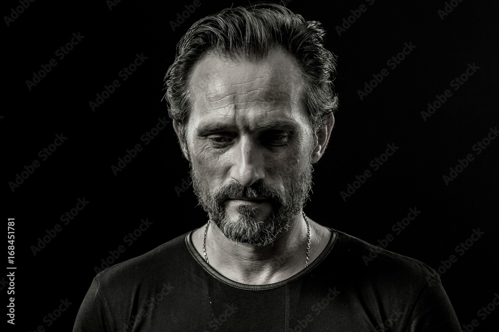Black and white close up portrait of a severe man with sad facial expression. Male showing painful emotion on a black background.