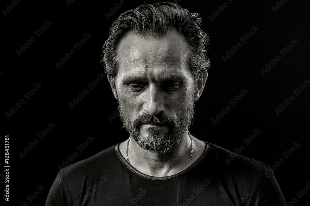Black and white close up portrait of a severe man with sad facial expression. Male showing painful emotion on a black background. Black and white close up portrait of a severe man with sad facial expression. Male showing painful emotion on a black background.