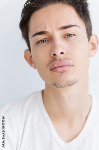 Portrait of a young man with dark hair and light eyes. on a white background. The guy in the white T-shirt. Male model.