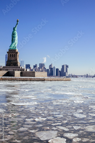 Statue of Liberty / Ellis Island surrounded by a frozen Hudson River; Downtown Manhattan skyline in background
