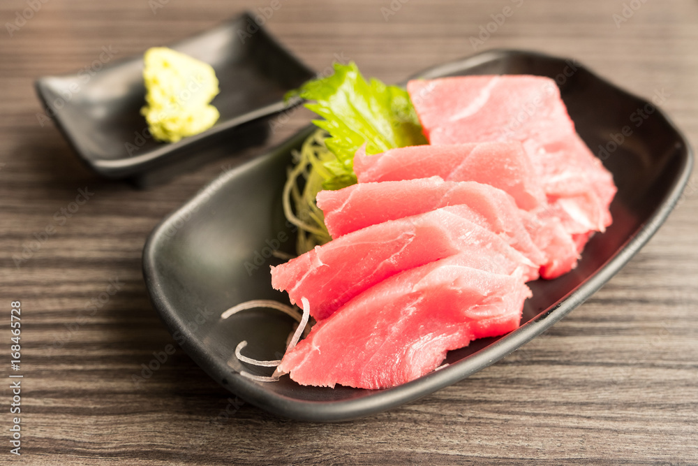 Tuna sashimi and wasabi in brown ceramic plate on wood table.