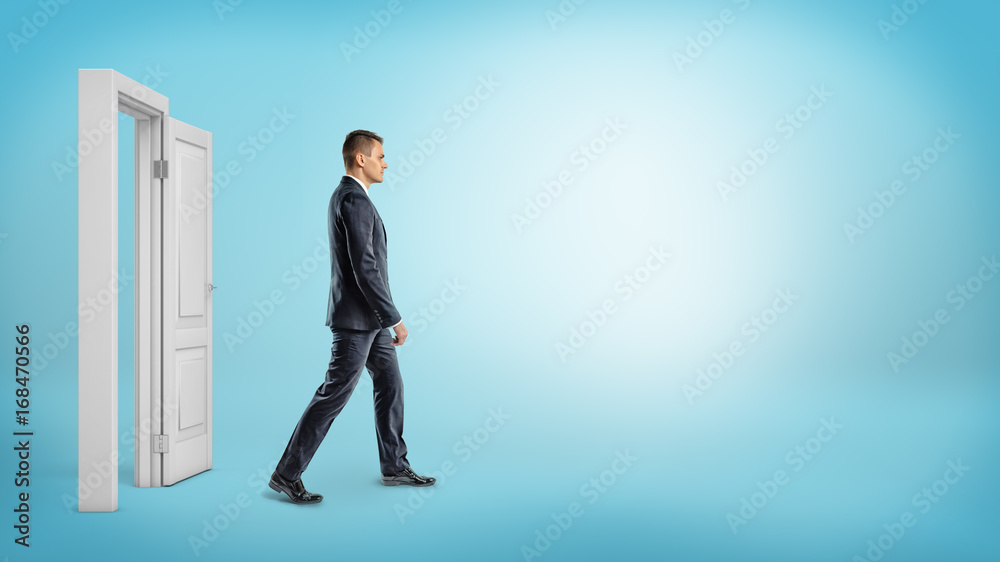 A businessman on blue background walking through an open white doorframe.
