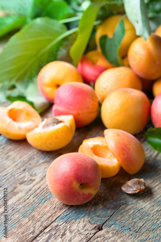 Juicy fresh apricots with leaves on old wooden table .