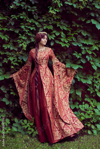 Beautiful Isabella of France, queen of England on Middle Ages period in red gown near medieval castle