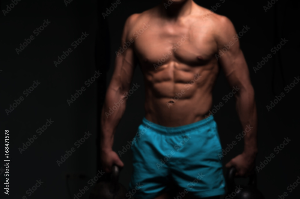 Fototapeta premium Male fitness model with kettle bells in hands