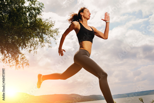 A beautiful sporty woman runing on the shore of a lake in sportswear. Girl is exercising photo