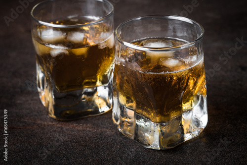 Whiskey with ice in glass on dark stone table.