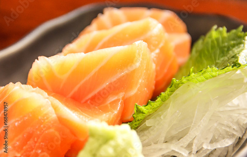Japanese food: salmon sashimi (fresh raw salmon meat) decorated with grated turnip and mint leaf on wooden table as a background.