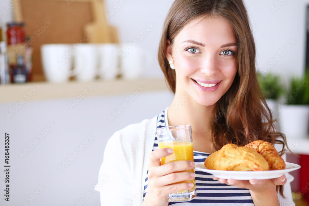 Young woman with glass of juice and cakes standing in kitchen Young woman with glass of juice and cakes standing in kitchen
