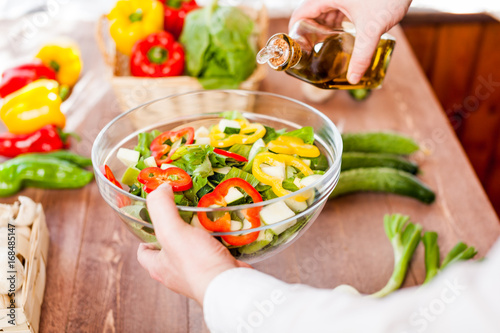 man pouring olive oil into healthy salad on kitchen