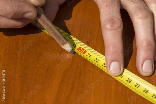 Dłoń robotnika oznacza punkt na desce ołówkiem stolarskim.