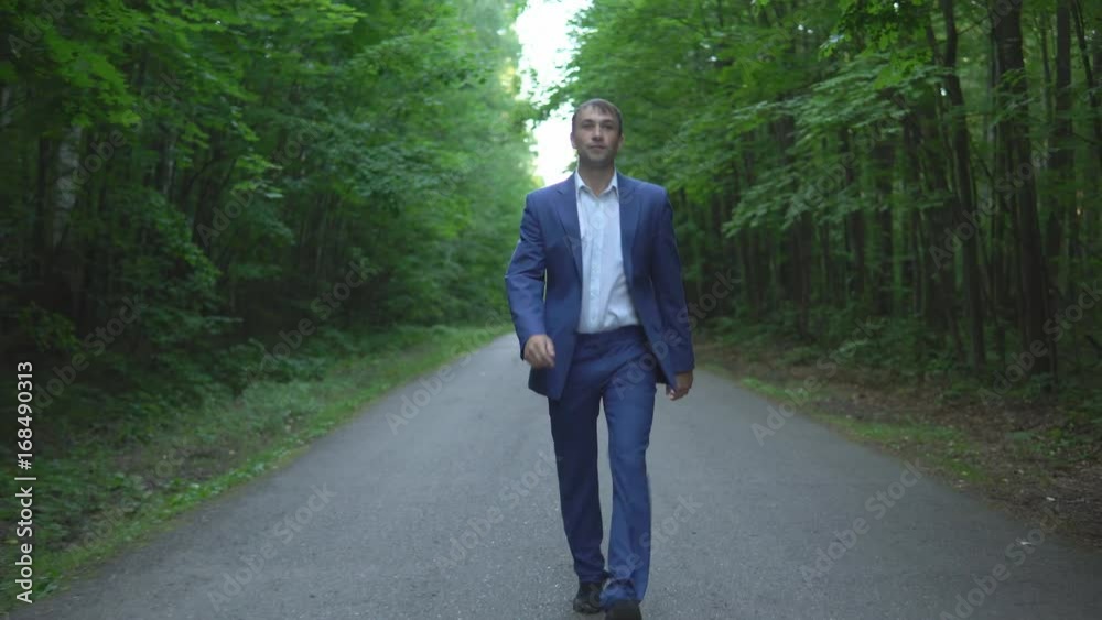 young businessman in a blue suit is walking along the road in forest young businessman in a blue suit is walking along the road in forest
