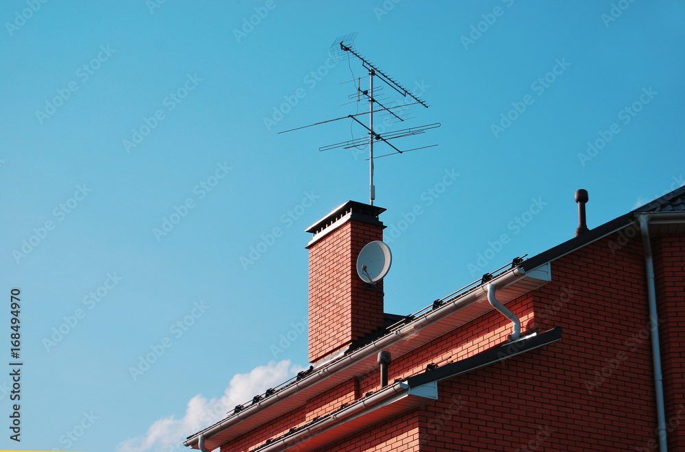 Part of the roof of a brick house, with a pipe and TV antennas