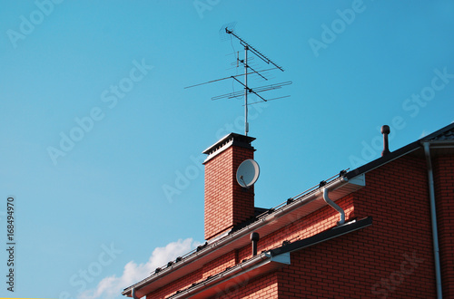 Part of the roof of a brick house, with a pipe and TV antennas