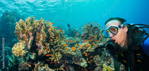 Underwater coral reef with man scuba diver exploring sea bottom.