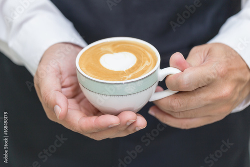 Barista holding cup of heart latte art coffee in cafe.