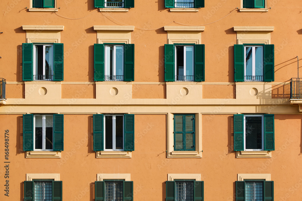 Part of the facade of an orange italian  building with windows with green shutters