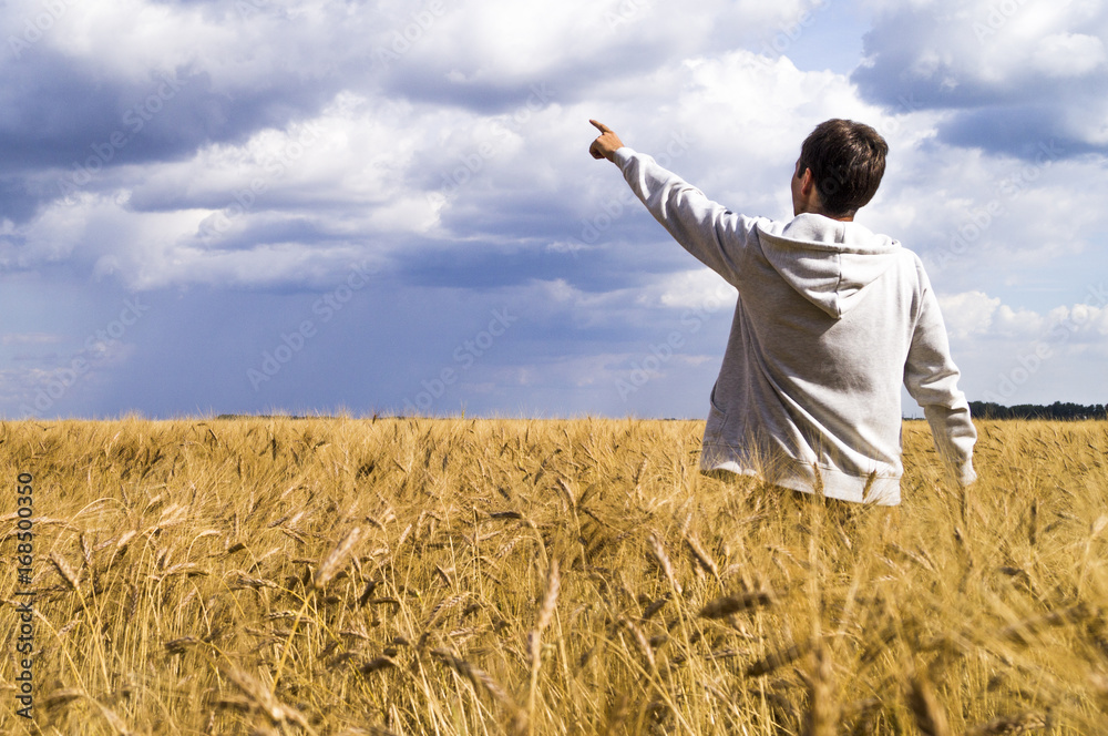 Man in a wheat field showing his fingers in the direction of the sky Man in a wheat field showing his fingers in the direction of the sky