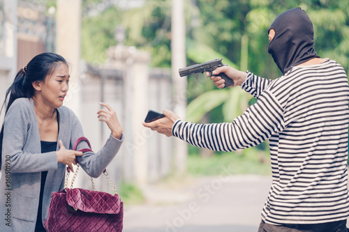 Man in hoodie robbing and threatening with gun to frightened young woman While talking on the phone. criminal and robbery for woman concept. photo